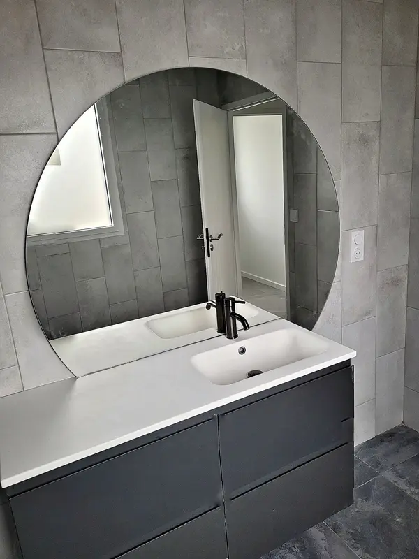 Salle de bain rénovée avec miroir rond, meuble vasque suspendu et prise électrique murale